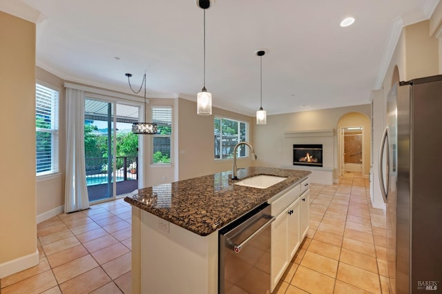 kitchen featuring light tile patterned flooring, a sink, stainless steel appliances, ornamental molding, and dark stone counters