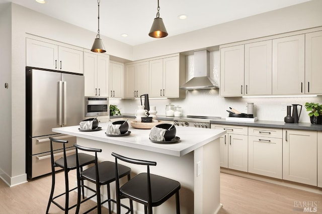 kitchen featuring a center island, wall chimney exhaust hood, stainless steel appliances, light hardwood / wood-style floors, and decorative light fixtures