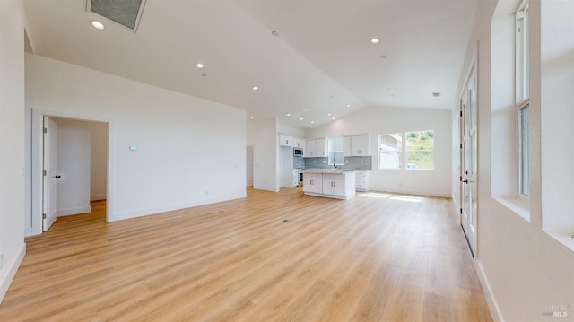 unfurnished living room featuring high vaulted ceiling, sink, and light hardwood / wood-style flooring