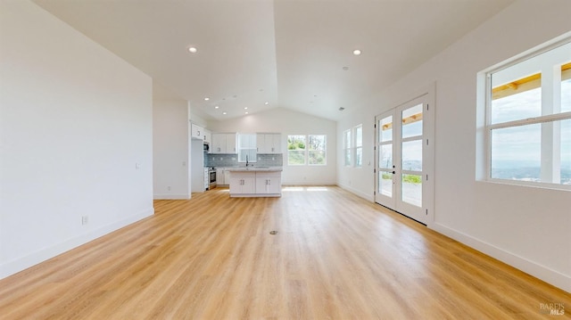 unfurnished living room with vaulted ceiling, sink, and light hardwood / wood-style flooring