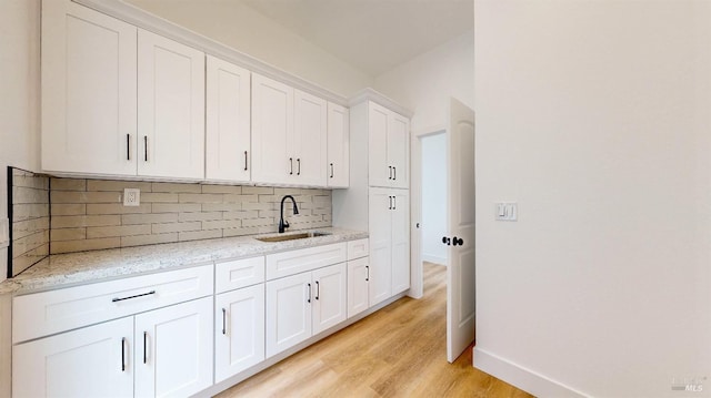 kitchen featuring sink, white cabinetry, light stone counters, light wood-type flooring, and decorative backsplash