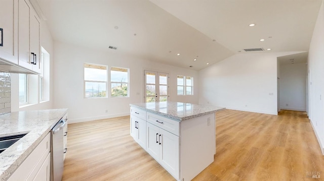 kitchen with vaulted ceiling, french doors, white cabinetry, light stone counters, and light hardwood / wood-style flooring