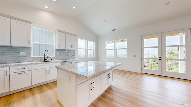 kitchen with a kitchen island, sink, white cabinets, light hardwood / wood-style floors, and light stone countertops