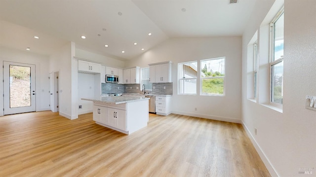 kitchen featuring light wood-type flooring, a kitchen island, stainless steel appliances, decorative backsplash, and white cabinets