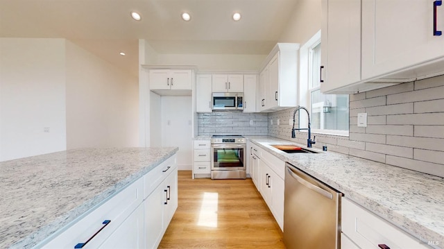 kitchen featuring sink, light stone counters, white cabinetry, light hardwood / wood-style flooring, and appliances with stainless steel finishes