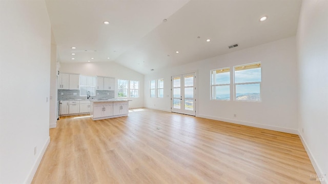 unfurnished living room featuring sink, vaulted ceiling, and light wood-type flooring