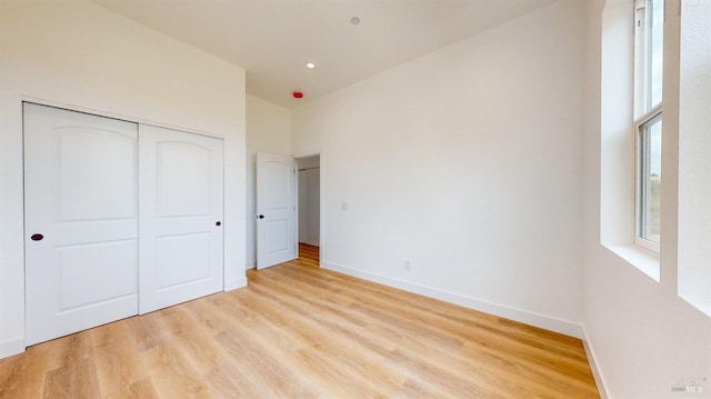 unfurnished bedroom with a towering ceiling, light hardwood / wood-style flooring, and a closet