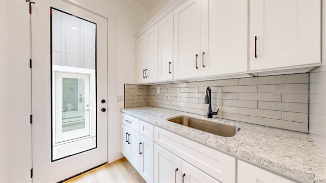 kitchen featuring sink, white cabinetry, tasteful backsplash, light stone countertops, and light hardwood / wood-style floors