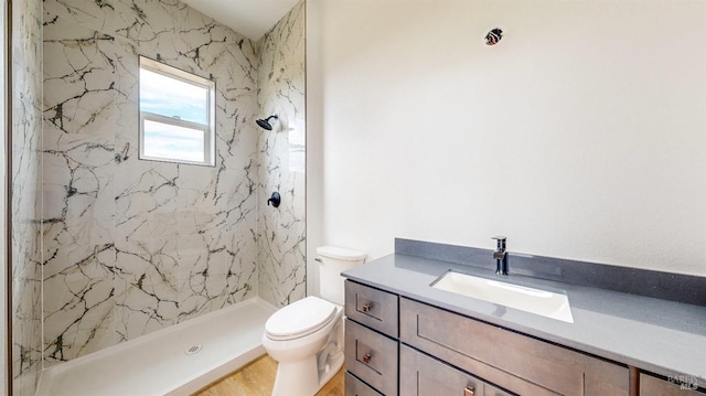 bathroom featuring vanity, wood-type flooring, toilet, and tiled shower