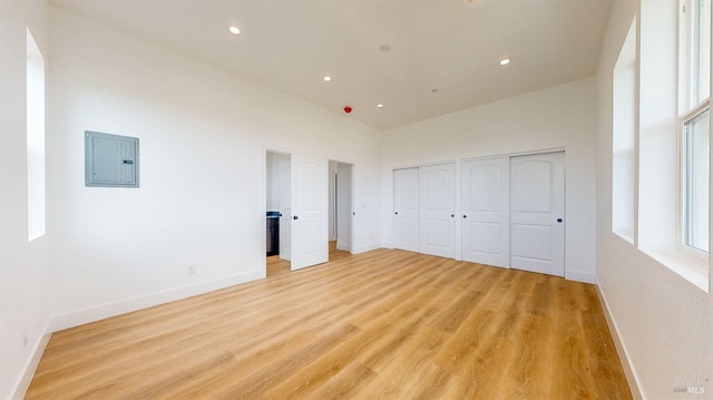 unfurnished bedroom with two closets, light hardwood / wood-style flooring, electric panel, and a towering ceiling