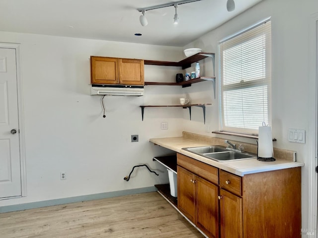 kitchen with a sink, baseboards, light wood-style floors, light countertops, and brown cabinets