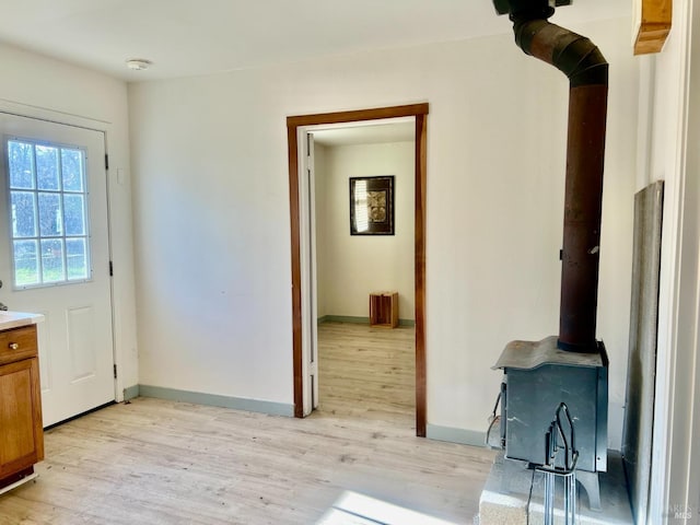 doorway with a wood stove, light wood finished floors, and baseboards