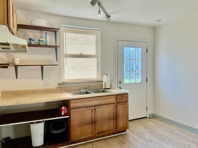 kitchen featuring a sink, baseboards, light countertops, light wood-type flooring, and brown cabinets