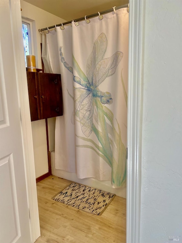 full bathroom with shower / tub combo, baseboards, and wood finished floors