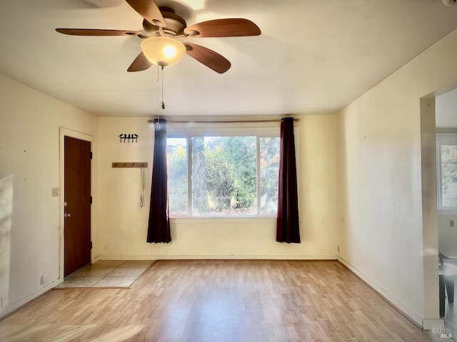 spare room featuring a ceiling fan, baseboards, and light wood finished floors