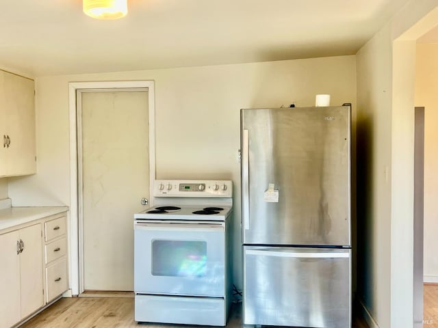 kitchen with light wood finished floors, white range with electric cooktop, light countertops, freestanding refrigerator, and white cabinetry