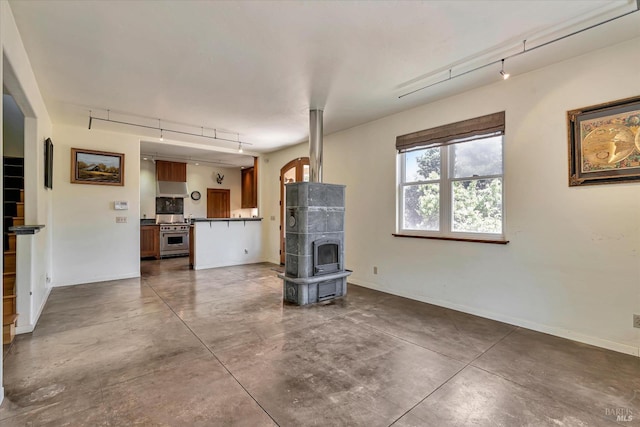 unfurnished living room with concrete flooring, baseboards, a wood stove, and track lighting