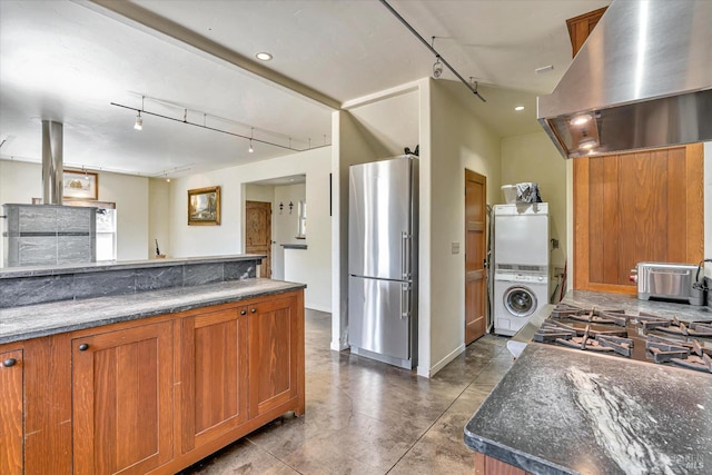 kitchen with stacked washer and dryer, island range hood, dark stone counters, brown cabinets, and freestanding refrigerator