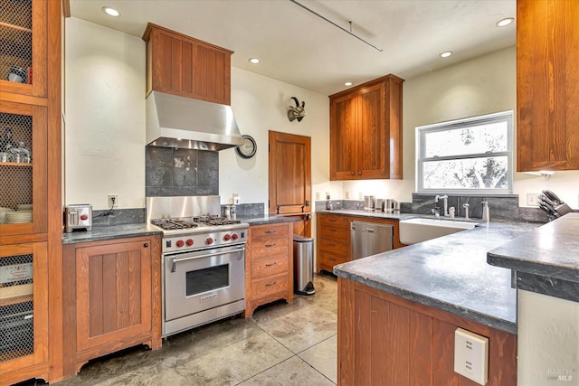 kitchen with dark countertops, appliances with stainless steel finishes, glass insert cabinets, a sink, and exhaust hood