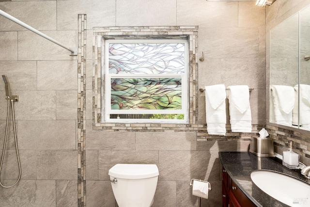 bathroom with tiled shower, toilet, tile walls, and a healthy amount of sunlight