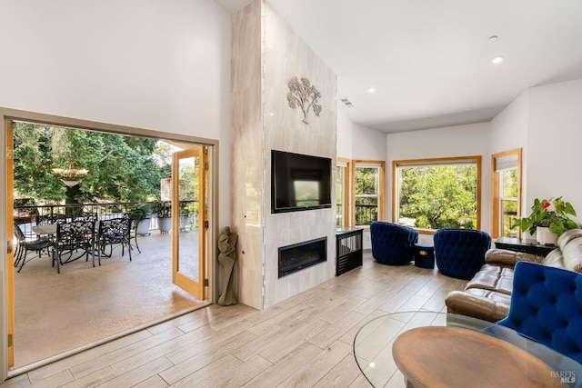 living room with a high end fireplace, a high ceiling, and light wood-type flooring