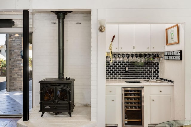 bar featuring backsplash, wine cooler, sink, white cabinetry, and a wood stove