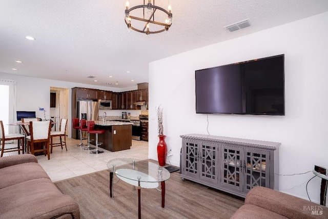 living room with sink, a chandelier, a textured ceiling, and light wood-type flooring