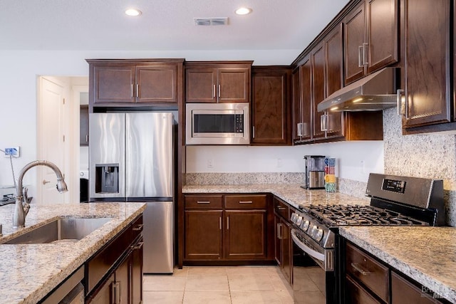 kitchen with light stone countertops, dark brown cabinets, stainless steel appliances, and sink