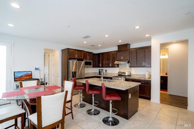 kitchen featuring light stone countertops, sink, a kitchen bar, a kitchen island with sink, and appliances with stainless steel finishes