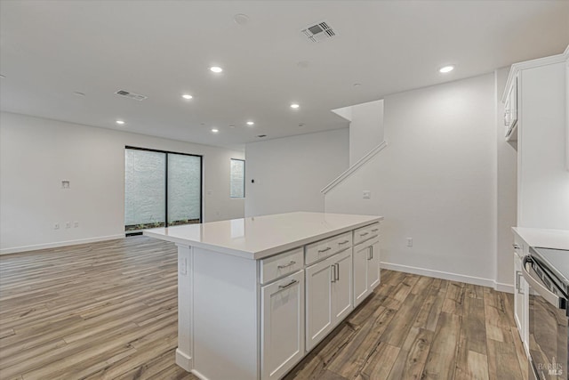 kitchen with white cabinetry, a center island, stainless steel range oven, and light wood-type flooring