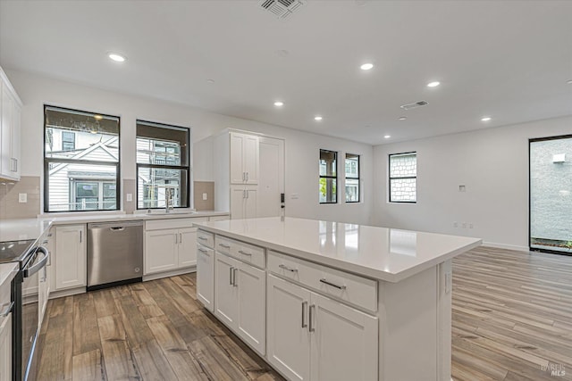 kitchen featuring backsplash, light wood-type flooring, appliances with stainless steel finishes, a kitchen island, and white cabinetry