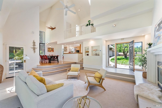 living room with a tile fireplace, a high ceiling, light colored carpet, and ceiling fan