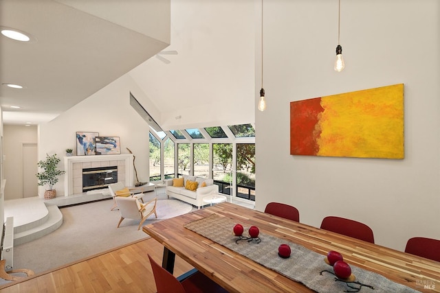 dining area featuring hardwood / wood-style floors, high vaulted ceiling, and a tile fireplace