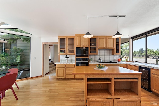 kitchen featuring rail lighting, a kitchen island, black appliances, wine cooler, and hanging light fixtures