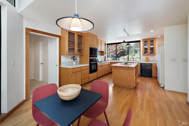 kitchen featuring light wood-type flooring, backsplash, black appliances, pendant lighting, and a center island