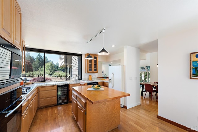 kitchen featuring white fridge with ice dispenser, beverage cooler, light hardwood / wood-style flooring, oven, and a kitchen island