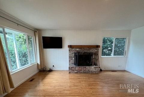 unfurnished living room with a brick fireplace, wood finished floors, and visible vents