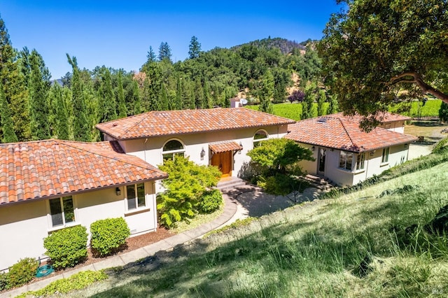 mediterranean / spanish house with stucco siding, a view of trees, and a tiled roof