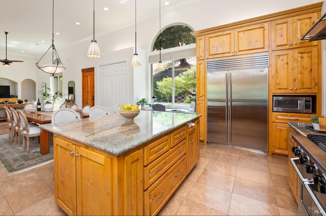 kitchen featuring arched walkways, a kitchen island, light stone counters, built in appliances, and hanging light fixtures