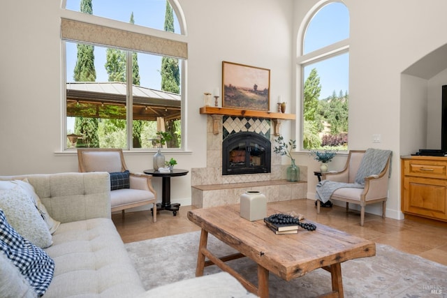 living area with light tile patterned flooring, a tiled fireplace, a towering ceiling, and baseboards