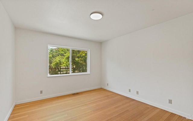 empty room featuring visible vents, light wood-style flooring, and baseboards