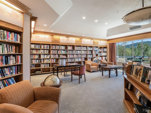 living area with built in shelves, light colored carpet, and a raised ceiling