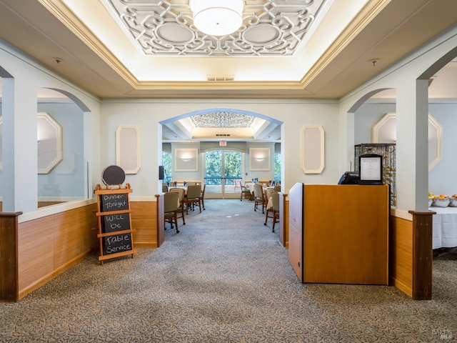 corridor featuring dark colored carpet, crown molding, and a tray ceiling