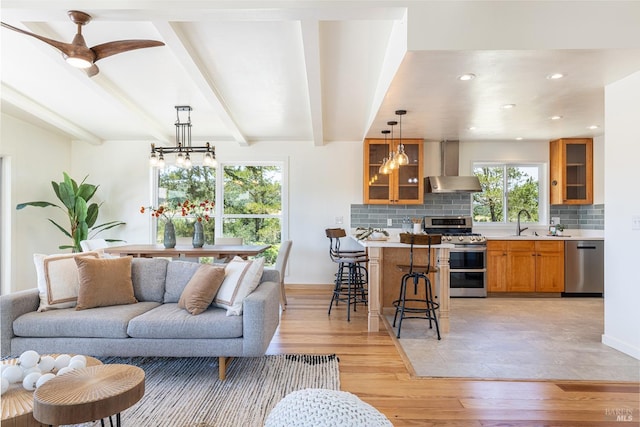 living room featuring vaulted ceiling with beams, light hardwood / wood-style floors, ceiling fan with notable chandelier, and a tiled fireplace