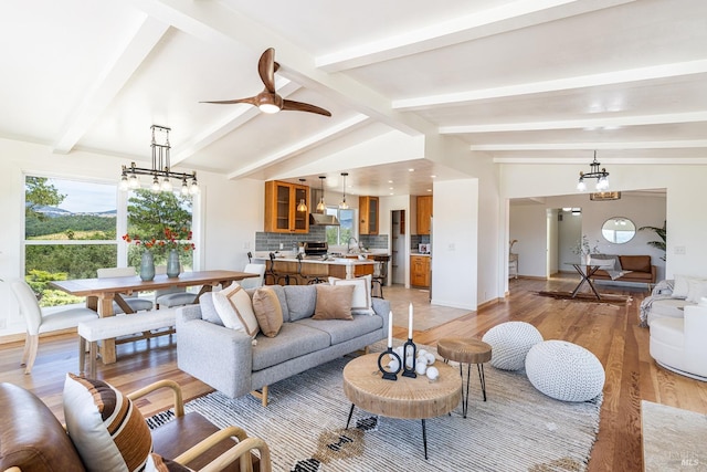 living room featuring vaulted ceiling with beams, ceiling fan with notable chandelier, and light hardwood / wood-style flooring