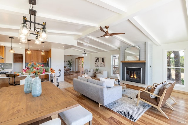 living room with lofted ceiling with beams, ceiling fan, a large fireplace, and light hardwood / wood-style floors