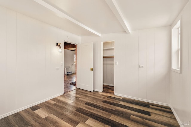 unfurnished bedroom with a spacious closet, a closet, dark hardwood / wood-style flooring, and beam ceiling