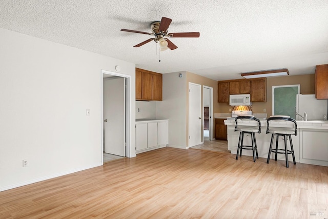 kitchen featuring white appliances, light hardwood / wood-style flooring, ceiling fan, a textured ceiling, and a kitchen bar