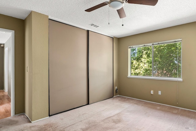 unfurnished bedroom with a textured ceiling, light colored carpet, and ceiling fan