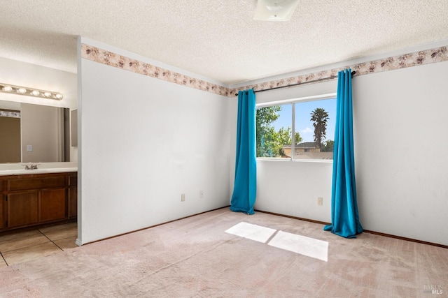 unfurnished bedroom with sink, connected bathroom, light colored carpet, and a textured ceiling